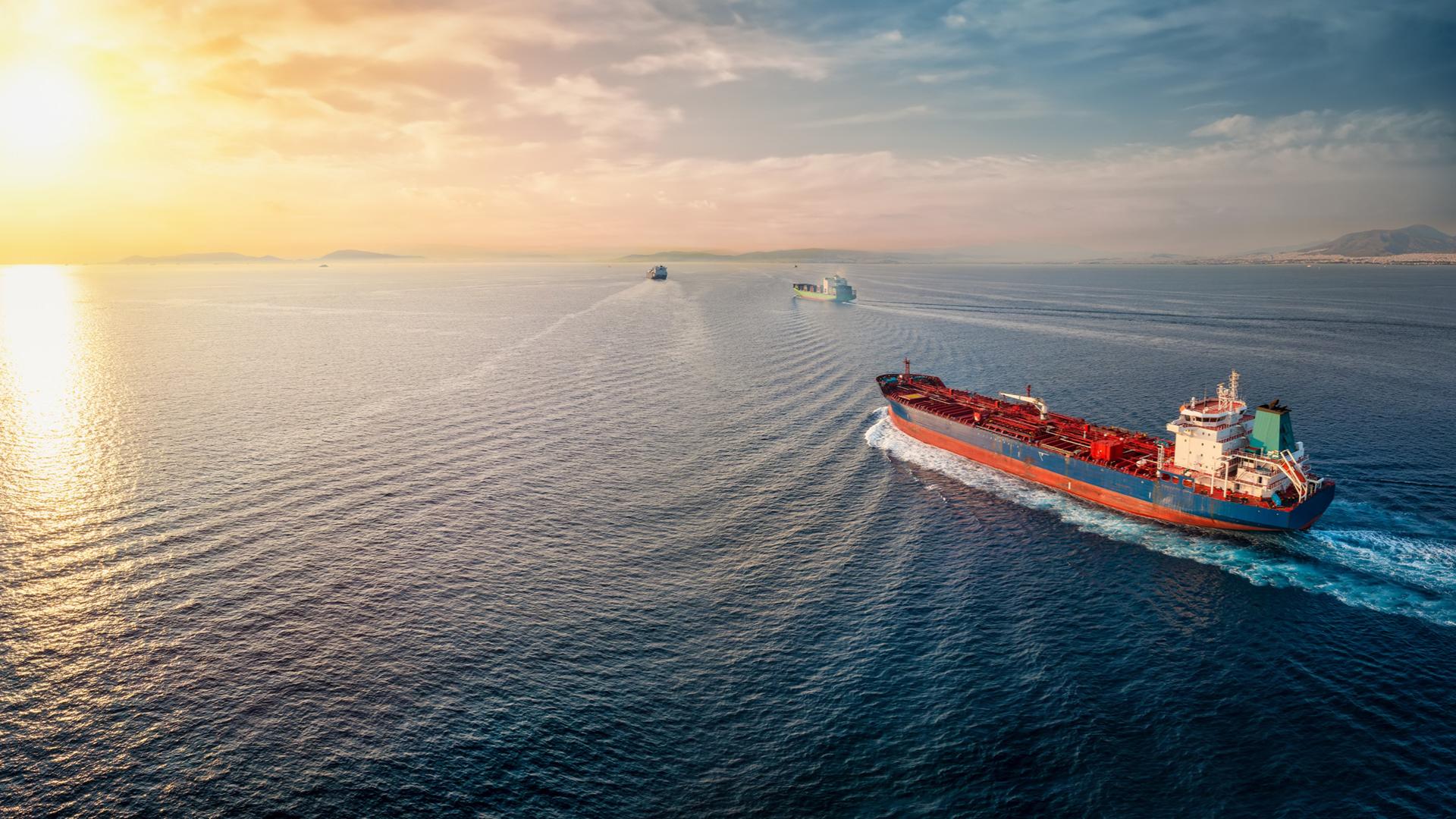 Nave cargo naviga al tramonto su un mare calmo, scortata da altre imbarcazioni.