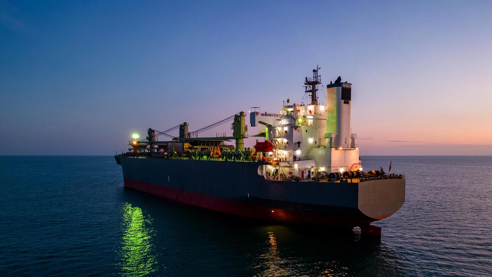 Grande nave cargo illuminata al tramonto sul mare calmo.