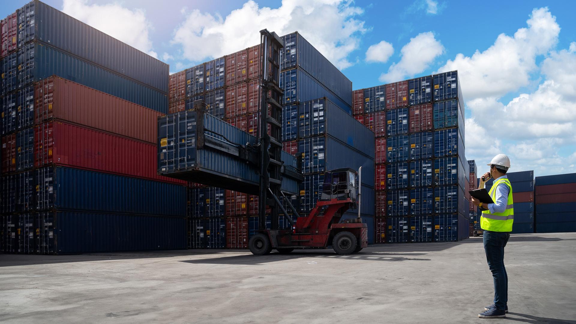 Operatore controlla container in porto con carrello elevatore.